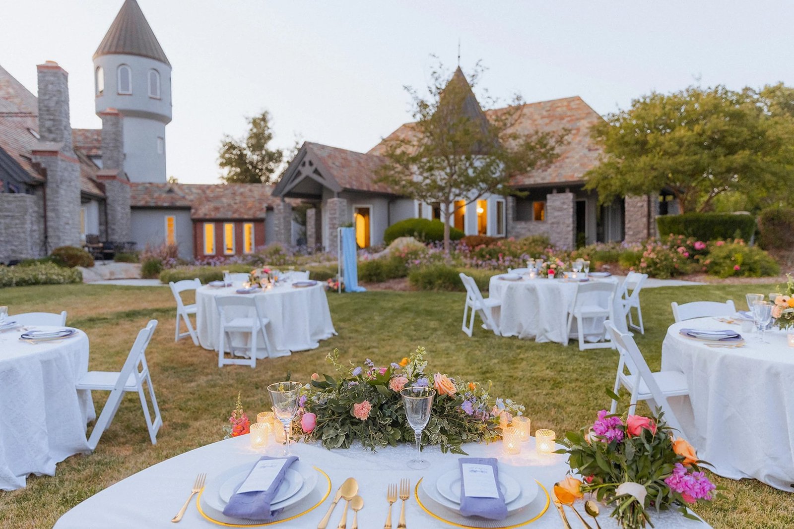 Round tables set for dinner on the lawn with the castle lit behind