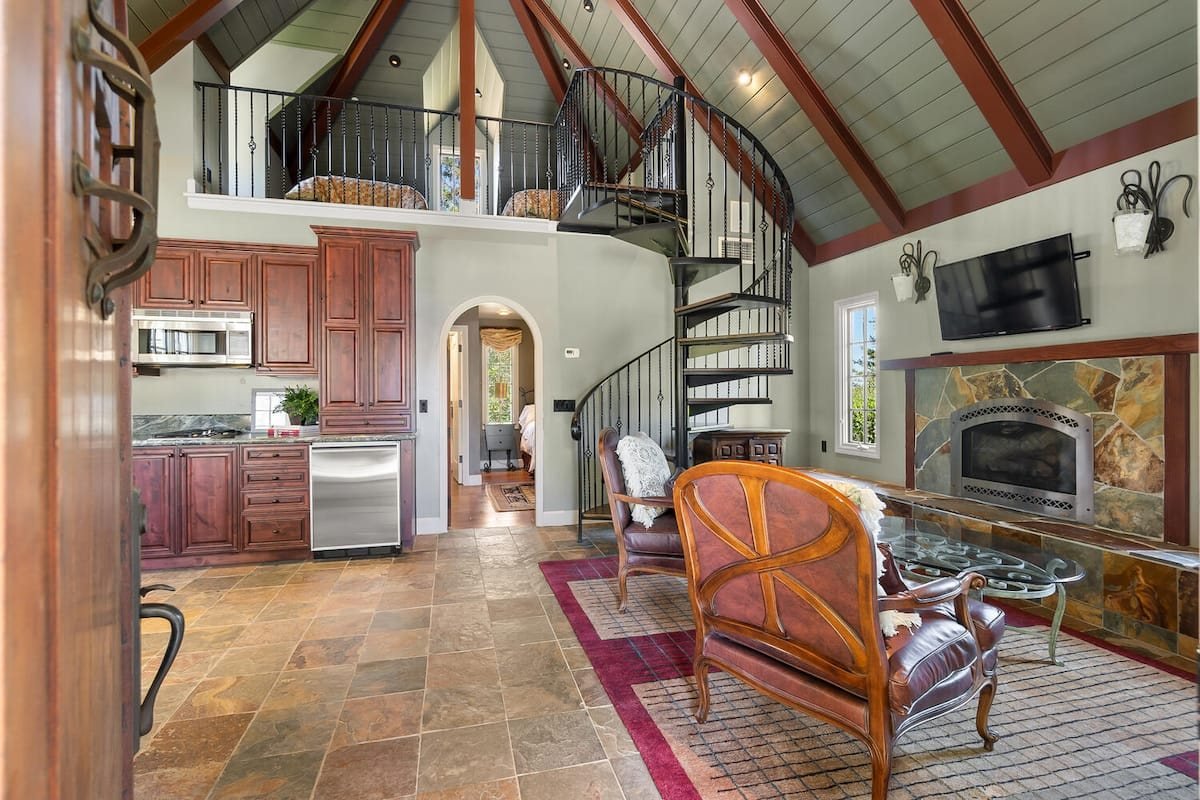 The retreat living room with vaulted beams, stone fireplace and spiral staircase to the loft